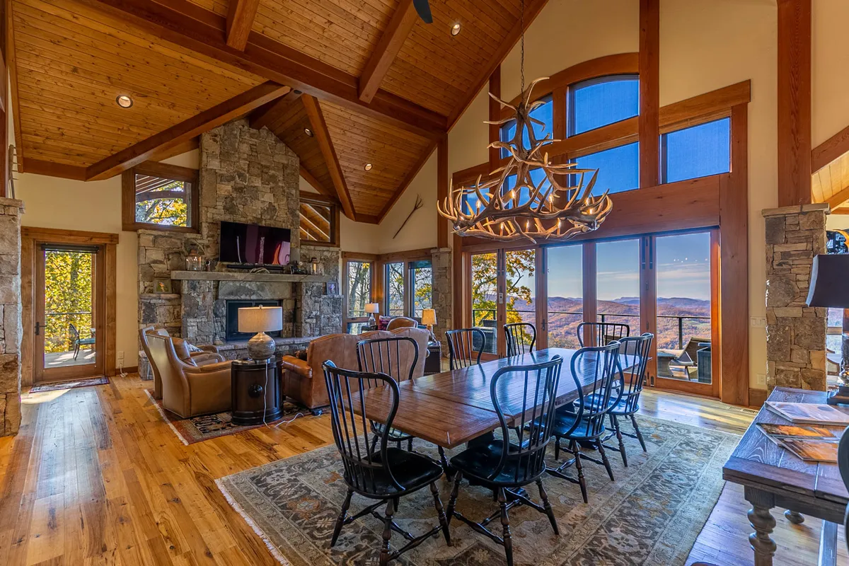 A large, inviting living and dining space with a prominent stone fireplace, a grand dining table perfect for groups, an elegant chandelier, and oversized windows offering mountain views. The setting is ideal for both intimate family gatherings and festive celebrations.