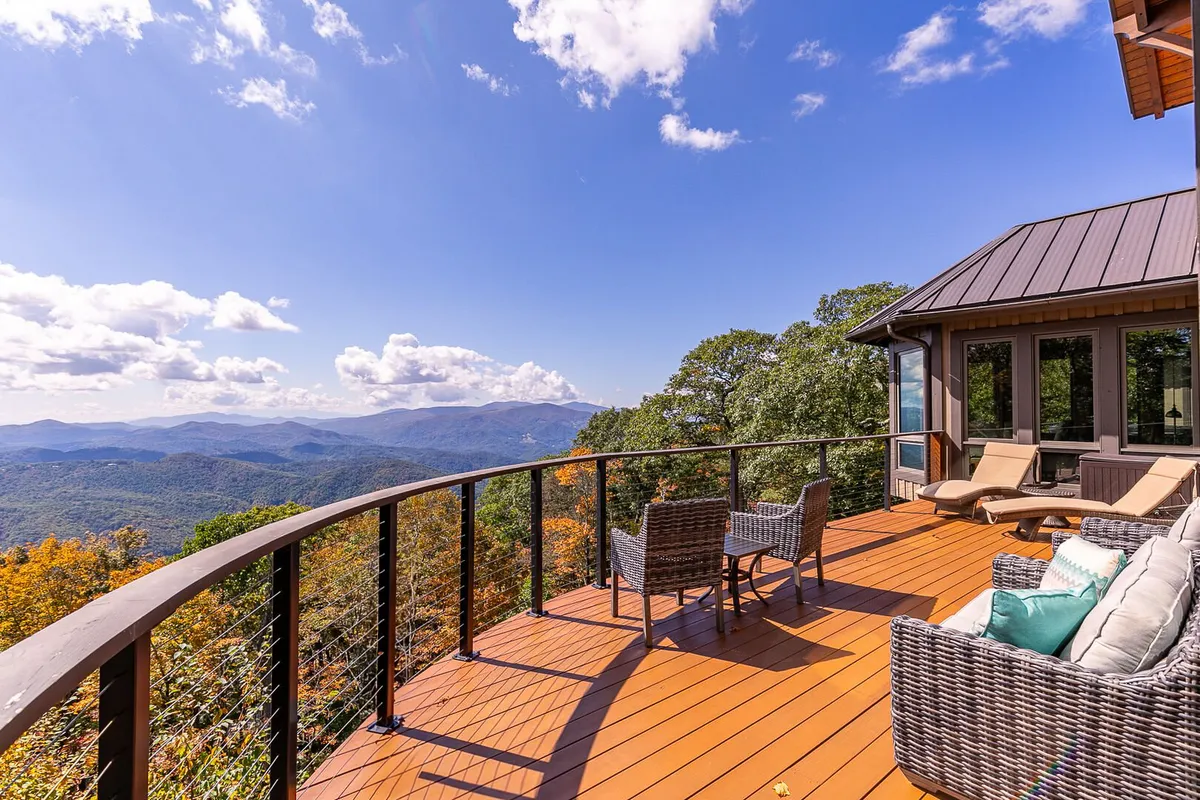This image captures an expansive wooden deck with comfortable outdoor seating, offering breathtaking panoramic mountain views. The scene is serene and inviting, with clear skies overhead and ample space for families to gather, relax, or snap memorable photos. The deck's vantage point underscores the property's mountain setting and the promise of al fresco breakfasts or evening barbecues.