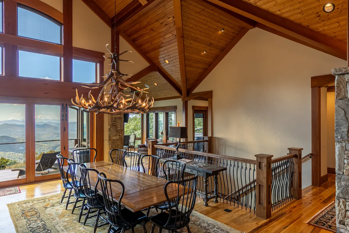An inviting dining area with a large wooden table beneath an antler chandelier, expansive windows flooding the space with natural light, and mountain views in the background. The setting is styled for intimate dinners and festive gatherings.