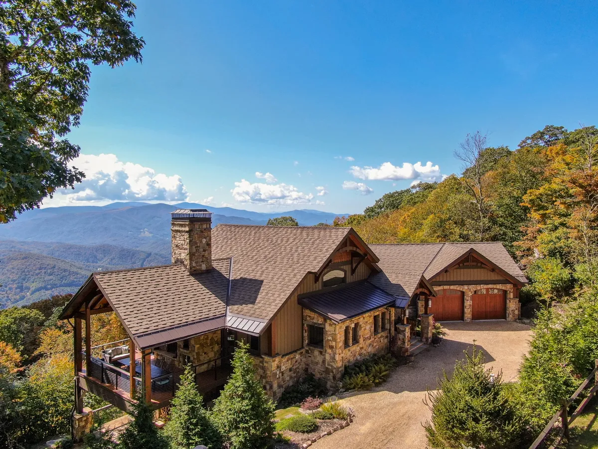 A tranquil exterior shot highlighting the stone facade and wooden porch, with expansive mountain views and surrounding greenery. The porch looks ready for gatherings, relaxation, or launching into nature trails.