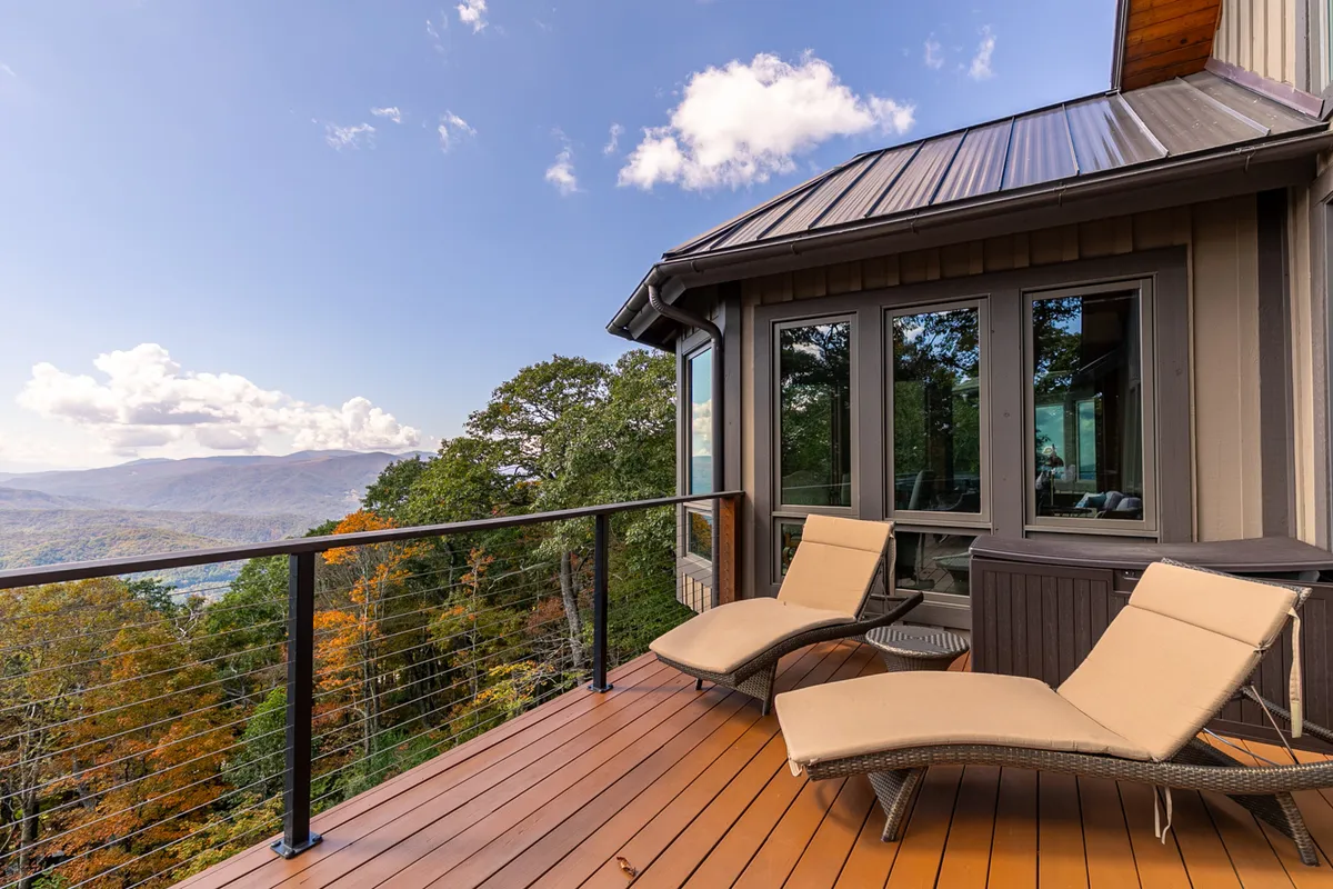 This image features a set of deck chairs positioned on a wooden deck with a glass railing, overlooking a sweeping mountain view. The soft morning light and subtle cloud cover create a tranquil setting, ideal for sunrise yoga or quiet moments immersed in nature.