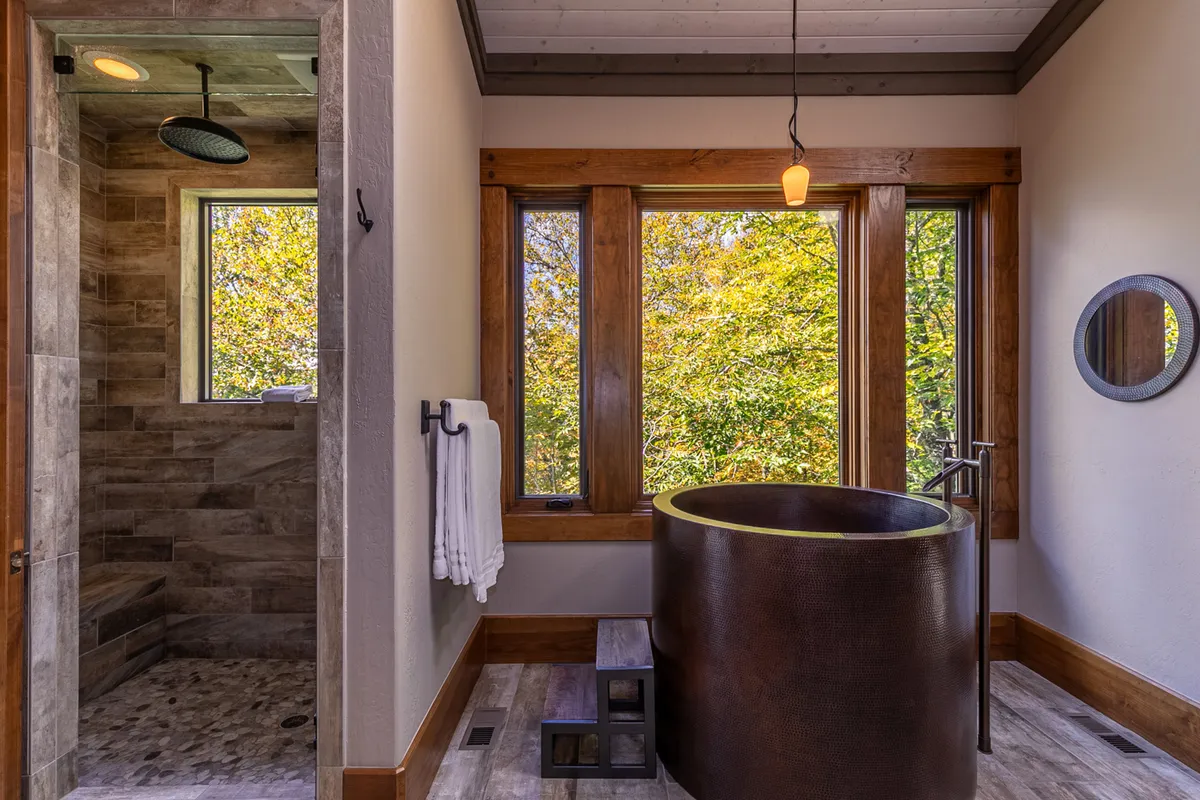 A spa-inspired bathroom with a freestanding tub placed near large windows that look out to nature. The space is accented with wood details and a modern shower area, exuding a sense of tranquility and rejuvenation.