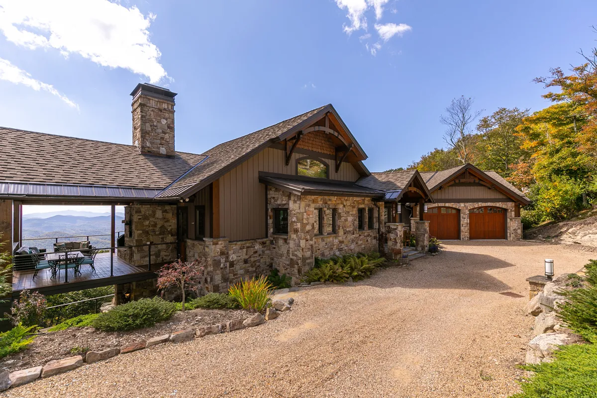 The exterior shot highlights the house's rustic stone facade and wooden accents, with a landscaped garden and a mountain view in the distance. The setting is welcoming and ideal for gathering outdoors, whether for morning coffee, evening stargazing, or group activities.