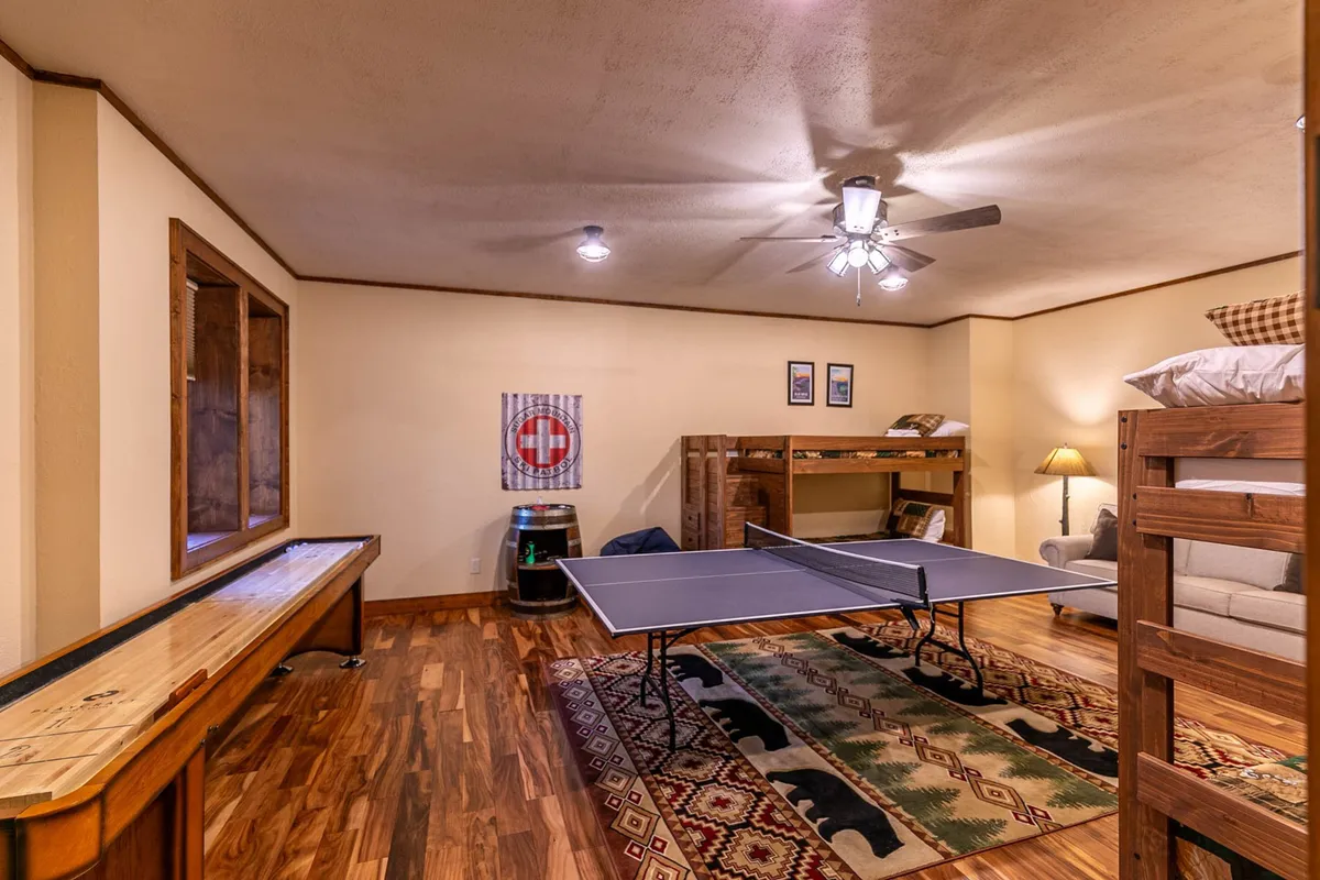 A multifunctional space with a ping pong table, bunk beds for lounging or napping, a plush sofa, and a rustic barrel accent. The room is designed for both active play and comfortable relaxation, offering plenty of options for fun and rest.