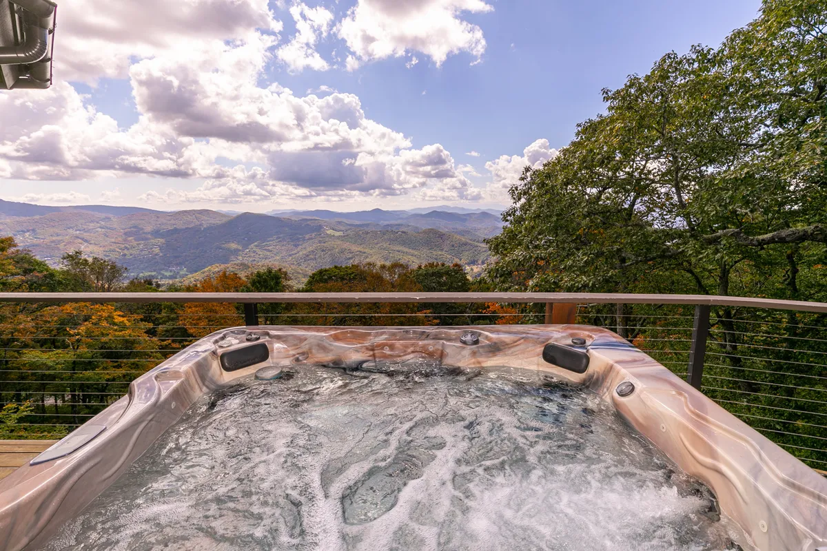 An outdoor hot tub set against a stunning mountain backdrop, with clouds drifting above. The tranquil scene invites relaxation, socializing, and stargazing after a day of mountain adventures.
